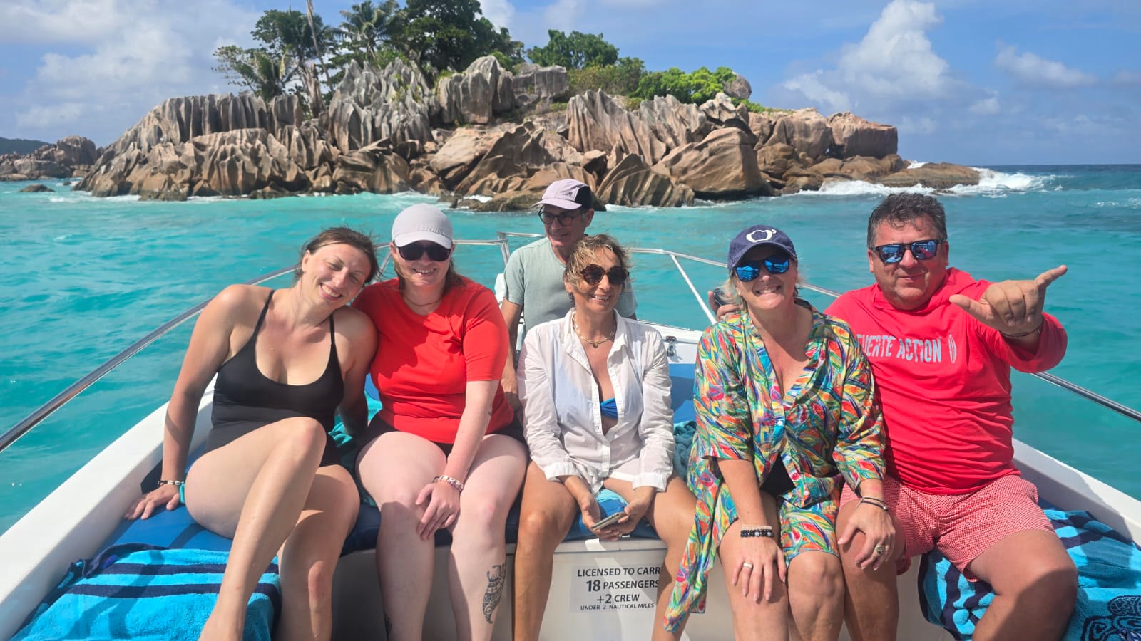 Guests sitting along the bow of Blue with granite boulders and palms behind them